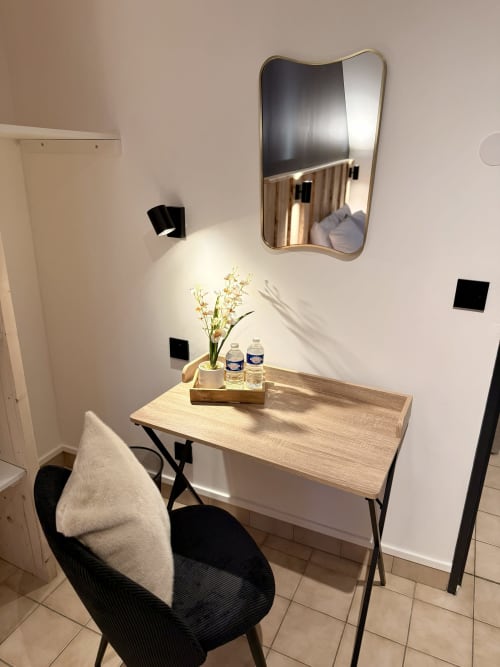 Bureau contemporain de l'Hôtel le tilleul avec miroir ondulé, surface bois, fleurs, bouteilles d'eau et chaise noire