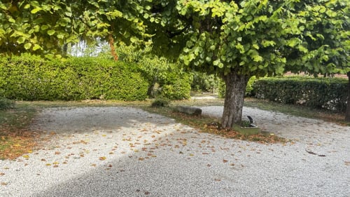 Shaded garden courtyard at Le Gite De Saint Phal with gravel pathways, mature trees, and manicured hedges in Saint-Phal