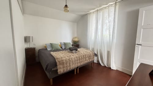 Bright bedroom at Le Gite De Saint Phal with queen bed, wooden nightstands, and white curtained windows overlooking the