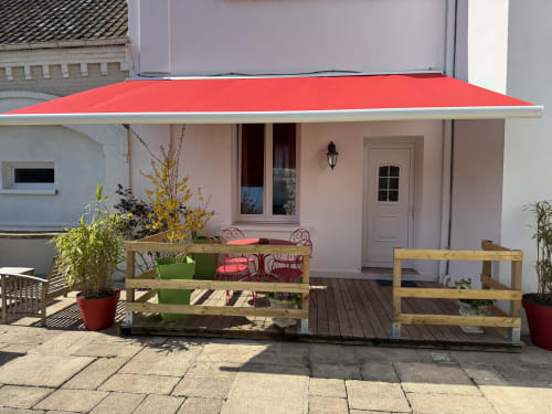 Red awning over patio seating at Au Bois Dormant cottage, Hesdin-la-Forêt garden view