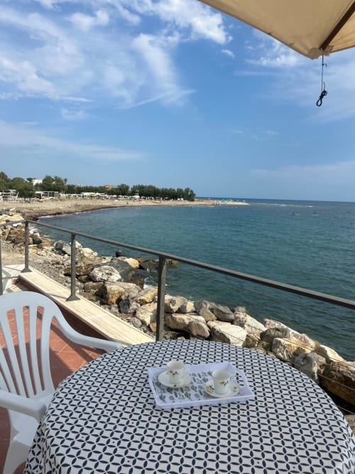 Cena in riva al mare a Villa Mareluce, Santa Marinella. Terrazza sul mare con vista panoramica, ombrelloni e costa rocciosa.
