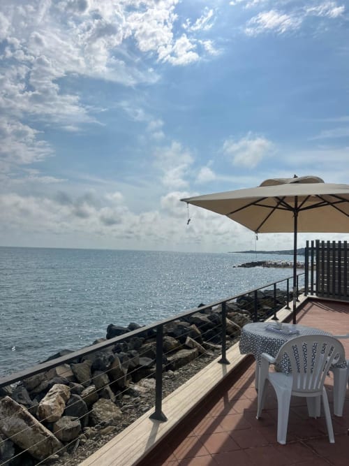Terrazza fronte mare della villa Casa Bella Pantheon a Santa Marinella con ombrellone, vista sul mare e sedie bianche