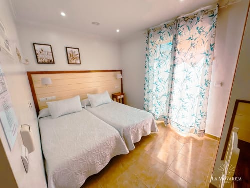 Habitación doble en Hostal La Moyareja de Rota con camas gemelas, cortinas florales y muebles de madera