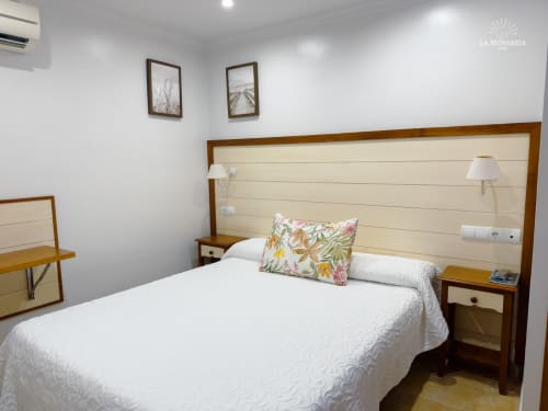 Luminosa habitación doble en el hostal La Moyareja de Rota con cama de madera, ropa de cama blanca y comodidades modernas