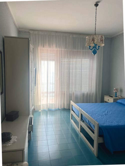 Camera da letto luminosa nella villa Casa Bella Pantheon a Santa Marinella con letto blu, vista sul mare, tende trasparenti e comfort moderni
