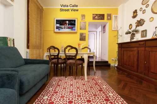 Luminoso soggiorno giallo in appartamento veneziano con tavolo da pranzo, divano turchese, mobili in legno e tappeto rosso fantasia