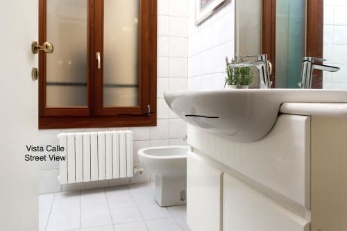 Bagno moderno in lussuoso appartamento veneziano con lavabo da appoggio, sanitari, radiatore e piastrelle in marmo