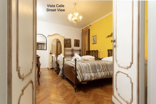 Camera da letto lussuosa a Venezia con letti gemelli, parete gialla, elegante lampadario e pavimenti in legno presso Luxury Loft