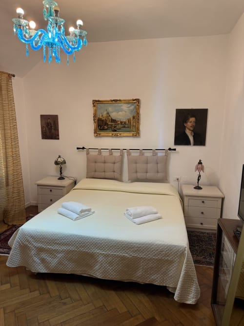 Camera da letto elegante nel Luxury Loft Venezia con letto matrimoniale, lampadario Murano blu, opere d'arte classiche e comodini beige