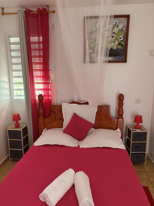 Chambre rouge et blanche avec lit en bois, voilages, tables de nuit et lampes à la villa L'ASETA PARADISE à Grand-Bourg