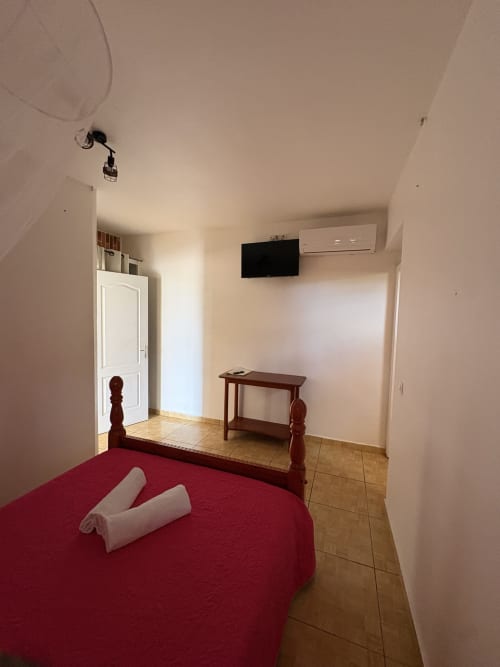 Chambre moderne de la villa La Maison Ihy à L'ASETA PARADISE, Grand-Bourg avec lit rouge et télévision écran plat