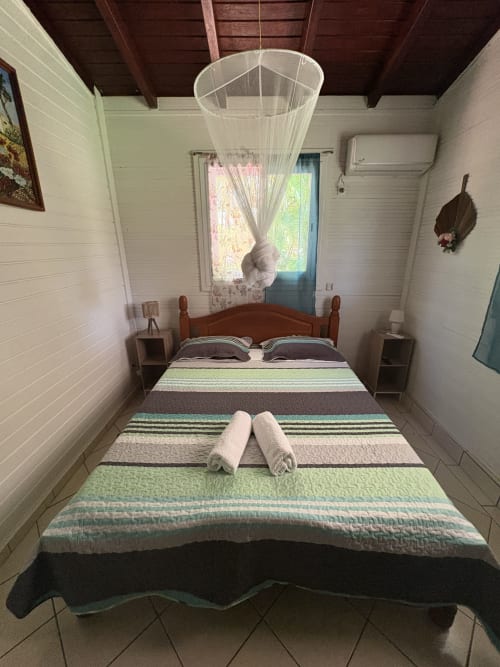 Chambre accueillante à la villa L'ASETA PARADISE à Grand-Bourg avec literie rayée, moustiquaire et vue sur mer