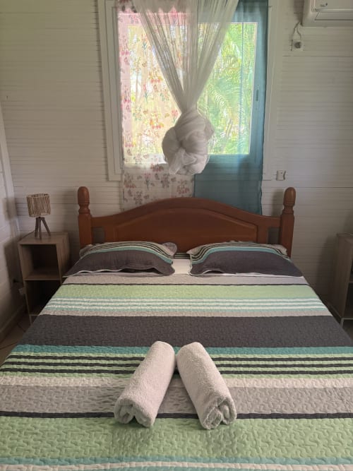 Chambre douillette à la villa L'ASETA PARADISE à Grand-Bourg avec literie rayée, serviettes roulées, lit en bois et vue sur le jardin