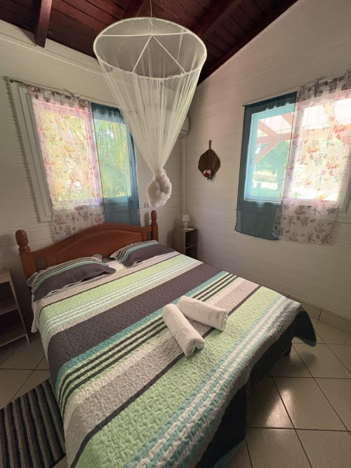 Chambre lumineuse de la villa L'Aseta Paradise avec literie rayée, moustiquaire, rideaux fleuris et vue sur mer à Grand-Bourg