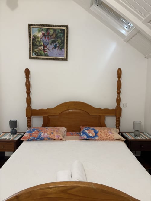 Chambre principale de la villa L'ASETA PARADISE à Grand-Bourg avec lit baldaquin en bois, draps blancs et coussins colorés
