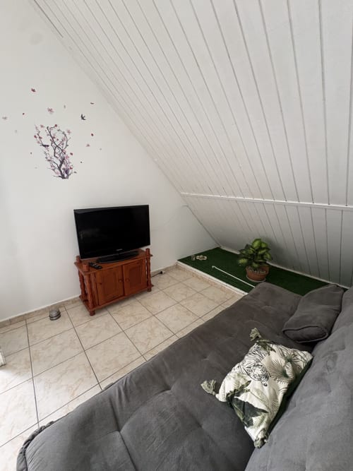 Chambre mansardée moderne avec canapé gris, meuble télé en bois et vue sur mer à la villa L'ASETA PARADISE, Grand-Bourg, Guadeloupe
