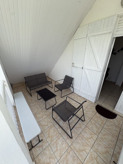 Coin lounge extérieur de la villa La Maison Mâat à Grand-Bourg avec chaises noires, bancs et table sur terrasse dallée