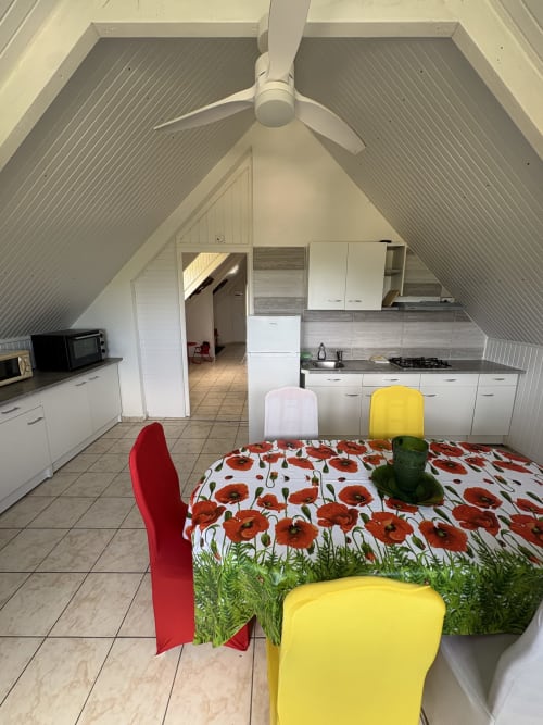 Salle à manger mansardée moderne avec chaises colorées, nappe à motif coquelicots et cuisine à la villa L'ASETA PARADISE, Grand-Bourg