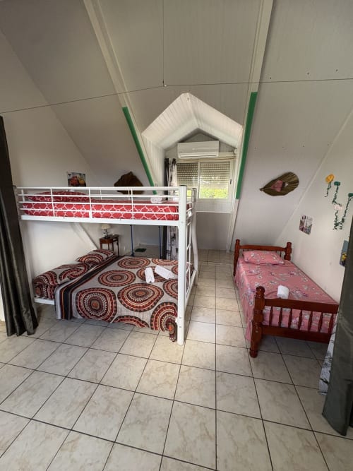 Chambre lumineuse de villa avec lits superposés blancs, literie à motifs rouges, carrelage et vue sur les montagnes à Grand-Bourg