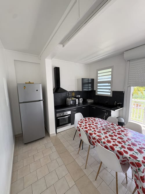 Cuisine moderne aux meubles noirs, table à manger avec nappe fleurie rouge et chaises blanches à la villa L'ASETA PARADISE