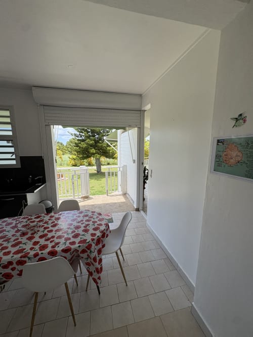 Cuisine-salle à manger lumineuse avec nappe à motif de pommes rouges, vue sur jardin par portes vitrées, villa L'Aseta Paradise, Grand-Bourg