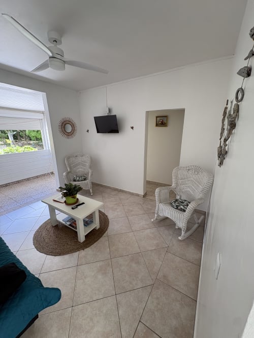 Séjour lumineux de la villa L'ASETA PARADISE à Grand-Bourg avec fauteuils en rotin, carrelage, TV murale et jardin