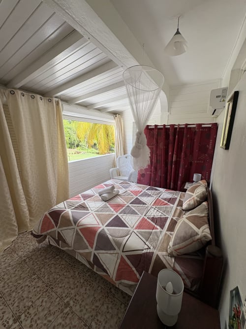 Chambre lumineuse de villa avec literie motifs géométriques, fenêtre vue jardin, rideaux crème et rideau cloisonneur bordeaux