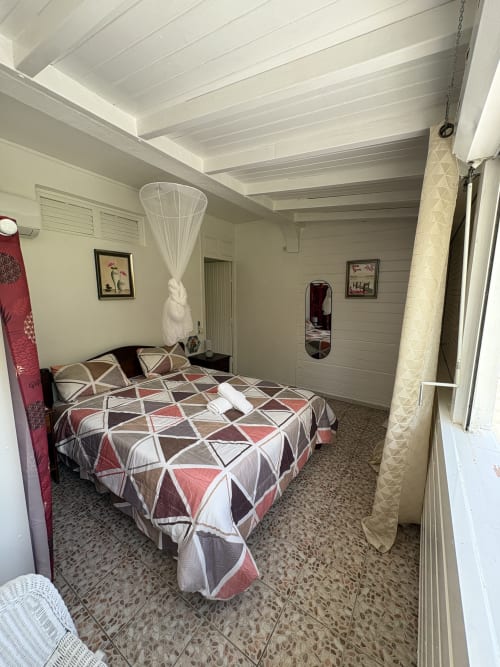 Spacieuse chambre de la villa L'ASETA PARADISE à Grand-Bourg avec lit queen-size, parure géométrique, poutres apparentes et vue jardin