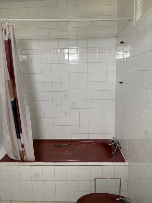 Salle de bain de la villa L'ASETA PARADISE à Grand-Bourg : carrelage blanc, baignoire rouge et rideau de douche