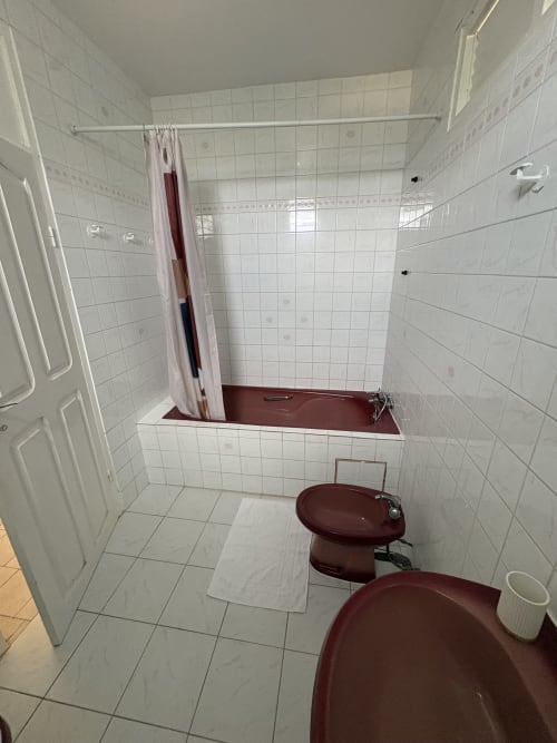 Salle de bain avec carrelage blanc, fixtures bourgogne, baignoire avec rideau de douche à la villa L'Aseta Paradise à Grand-Bourg