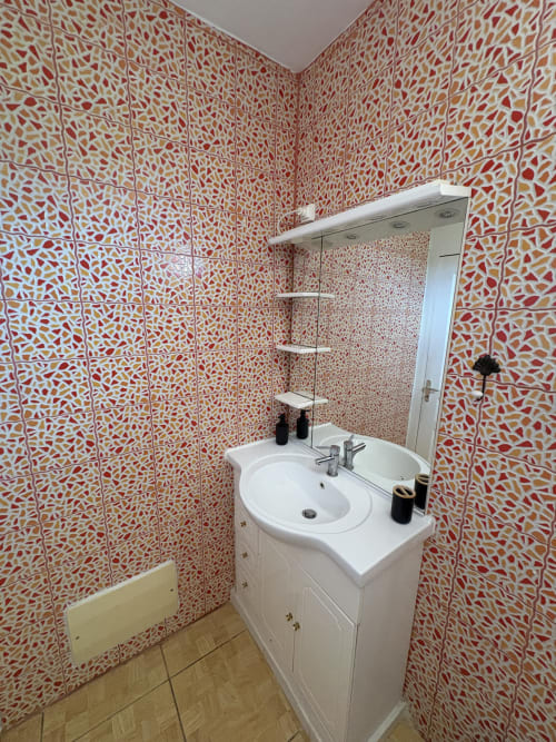 Salle de bain moderne avec carrelage à motifs rouge et orange, lavabo blanc et miroir à la villa L'ASETA PARADISE