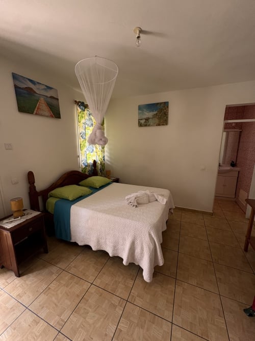 Chambre spacieuse de la villa L'ASETA PARADISE à Grand-Bourg avec lit en bois, oreillers verts, couvre-lit blanc et table de nuit