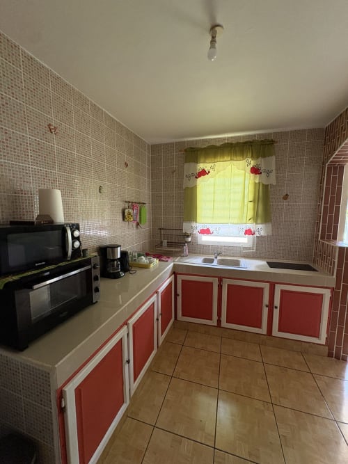 Cuisine lumineuse de la villa L'ASETA PARADISE avec armoires rouges et blanches, électroménagers modernes, carrelage rose et vue sur le jardin