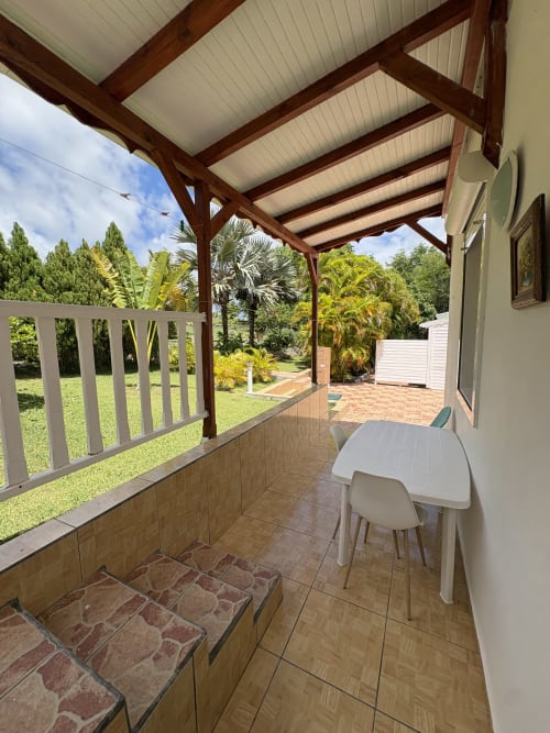 Terrasse couverte avec table de salle à manger blanche à la villa La Maison Meret, Grand-Bourg, donnant sur un jardin tropical luxuriant