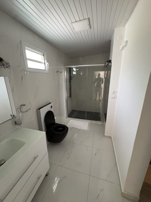 Salle de bain moderne de la villa L'ASETA PARADISE en Guadeloupe avec toilettes noires, cabine de douche et carrelage effet marbre