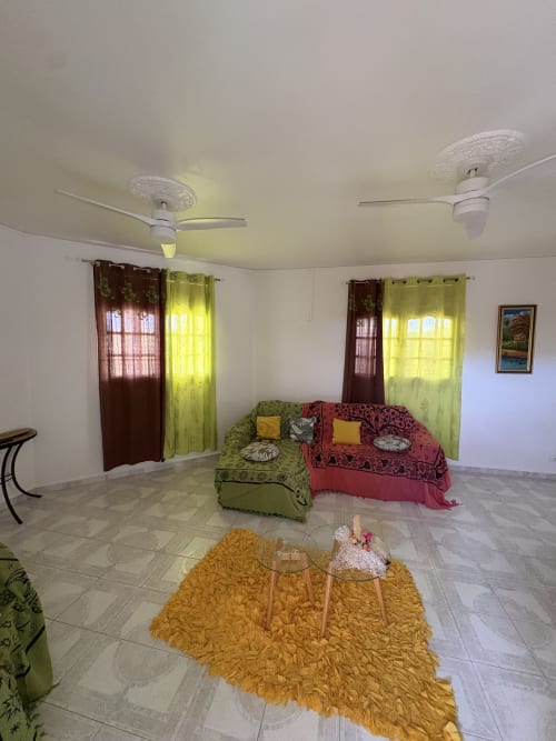 Spacieux séjour de la villa L'Aseta Paradise en Guadeloupe avec canapés verts et rouges, ventilateurs de plafond et vue sur le jardin