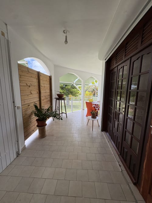 Vaste véranda couverte de la villa L'Aseta Paradise en Guadeloupe avec carrelage, volets en bois, portes foncées et jardin