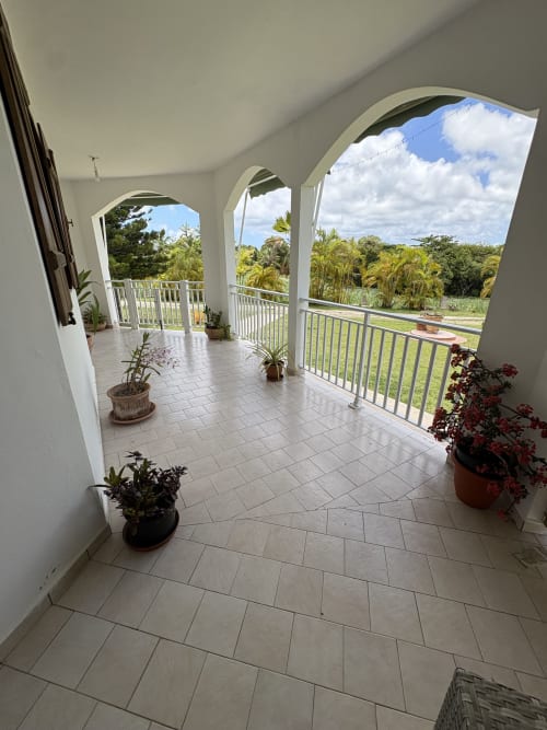 Terrasse couverte spacieuse de la villa L'ASETA PARADISE en Guadeloupe avec carrelage, balustrades blanches et plantes en pots