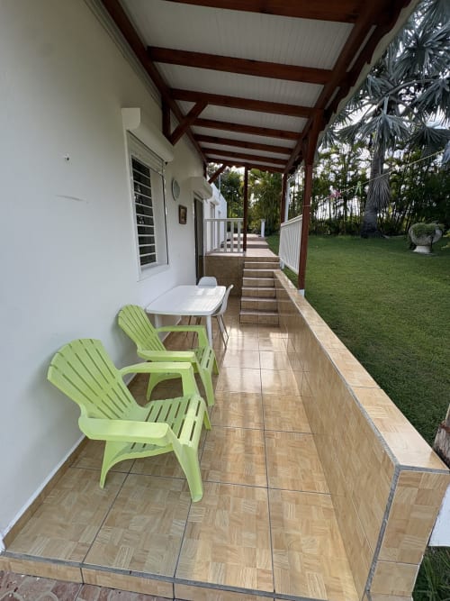 Terrasse couverte de la villa L'ASETA PARADISE à Grand-Bourg avec chaises vert citron, table blanche et vue sur le jardin
