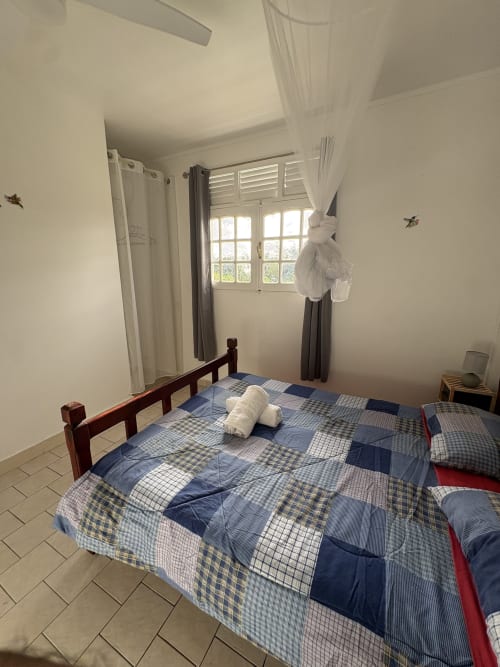 Chambre lumineuse avec literie patchwork bleue à la villa L'ASETA PARADISE à Grand-Bourg, Guadeloupe, vue sur jardin