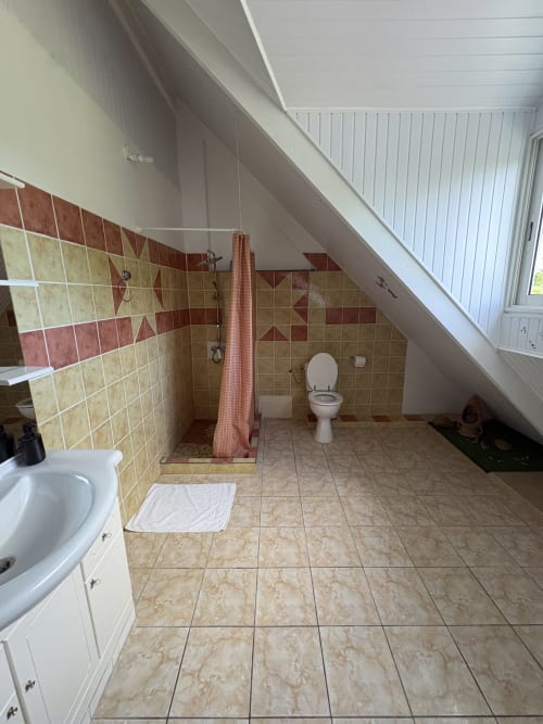 Salle de bains spacieuse mansardée à la villa L'ASETA PARADISE à Grand-Bourg avec douche carrelée, toilettes et plafond incliné