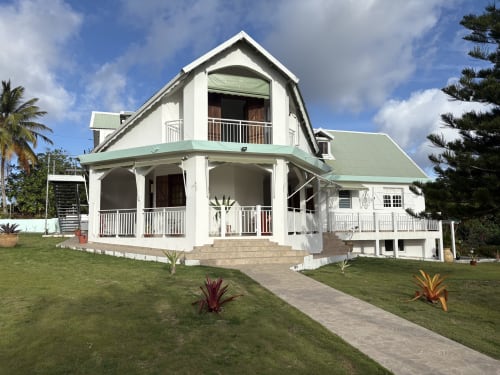 Villa L'ASETA PARADISE à Grand-Bourg, Guadeloupe. Maison coloniale blanche au toit vert, véranda circulaire, jardin soigné