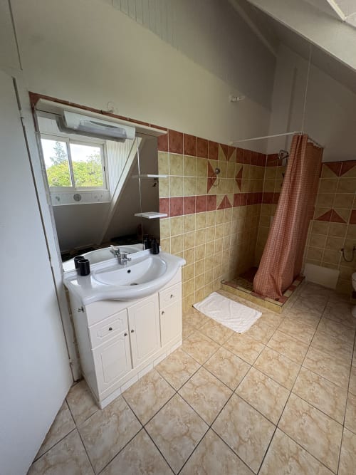 Salle de bains moderne à la villa L'ASETA PARADISE à Grand-Bourg avec lavabo blanc, murs carrelés, douche et vue sur fenêtre