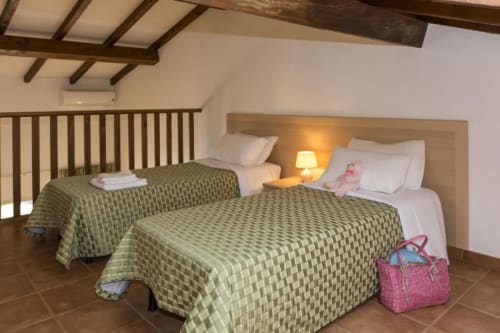 Chambre spacieuse du duplex avec lits jumeaux, poutres apparentes et luminosité chaleureuse à la Résidence SOGNU DI MARE à Linguizzetta