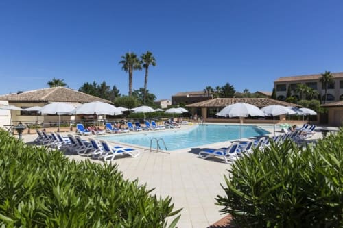 Espace piscine de la Résidence de Vacances SOGNU DI MARE à Linguizzetta avec transats bleus, parasols blancs et palmiers