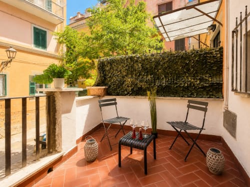 Terrazza soleggiata degli Appartamenti Castelli ad Albano Laziale con sedie nere, piante verdi e muri ricoperti di edera