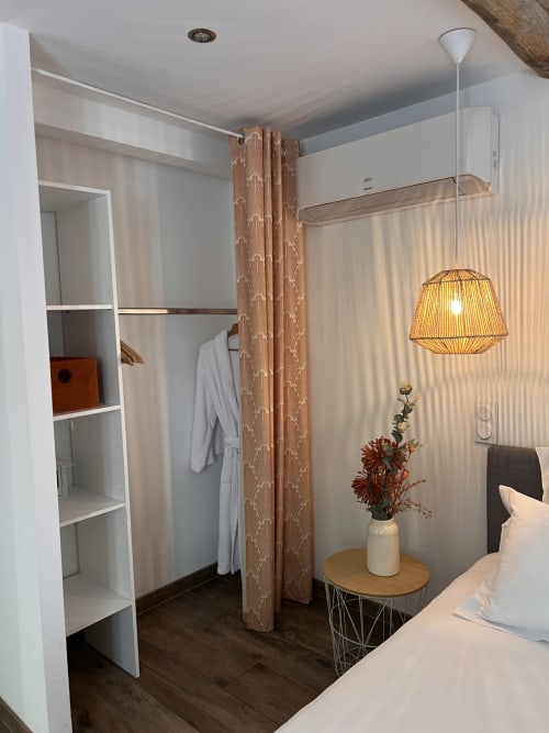 Chambre moderne à La Maison de Vaison B&B avec étagères blanches, rideau séparateur effet bois et luminaire suspendu en rotin