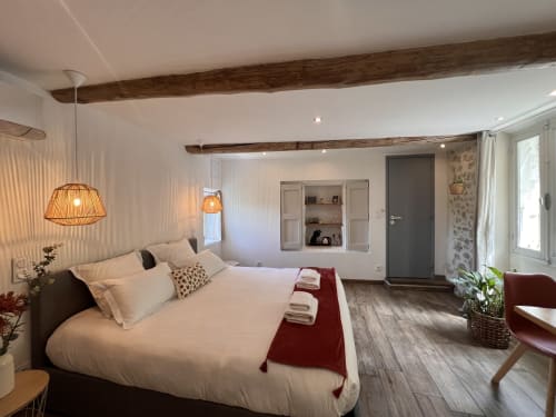 Chambre élégante à La Maison de Vaison avec literie blanche, poutres en bois rustique, éclairage suspendu et équipements modernes