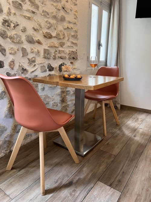Salle à manger moderne de la maison d'hôtes La Maison de Vaison avec murs en pierre, table en bois et chaises corail à Vaison-la-Romaine