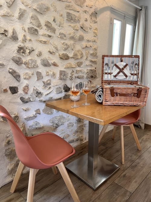 Coin repas accueillant à La Maison de Vaison avec mur en pierre brute, table en bois, chaise corail et panier pique-nique